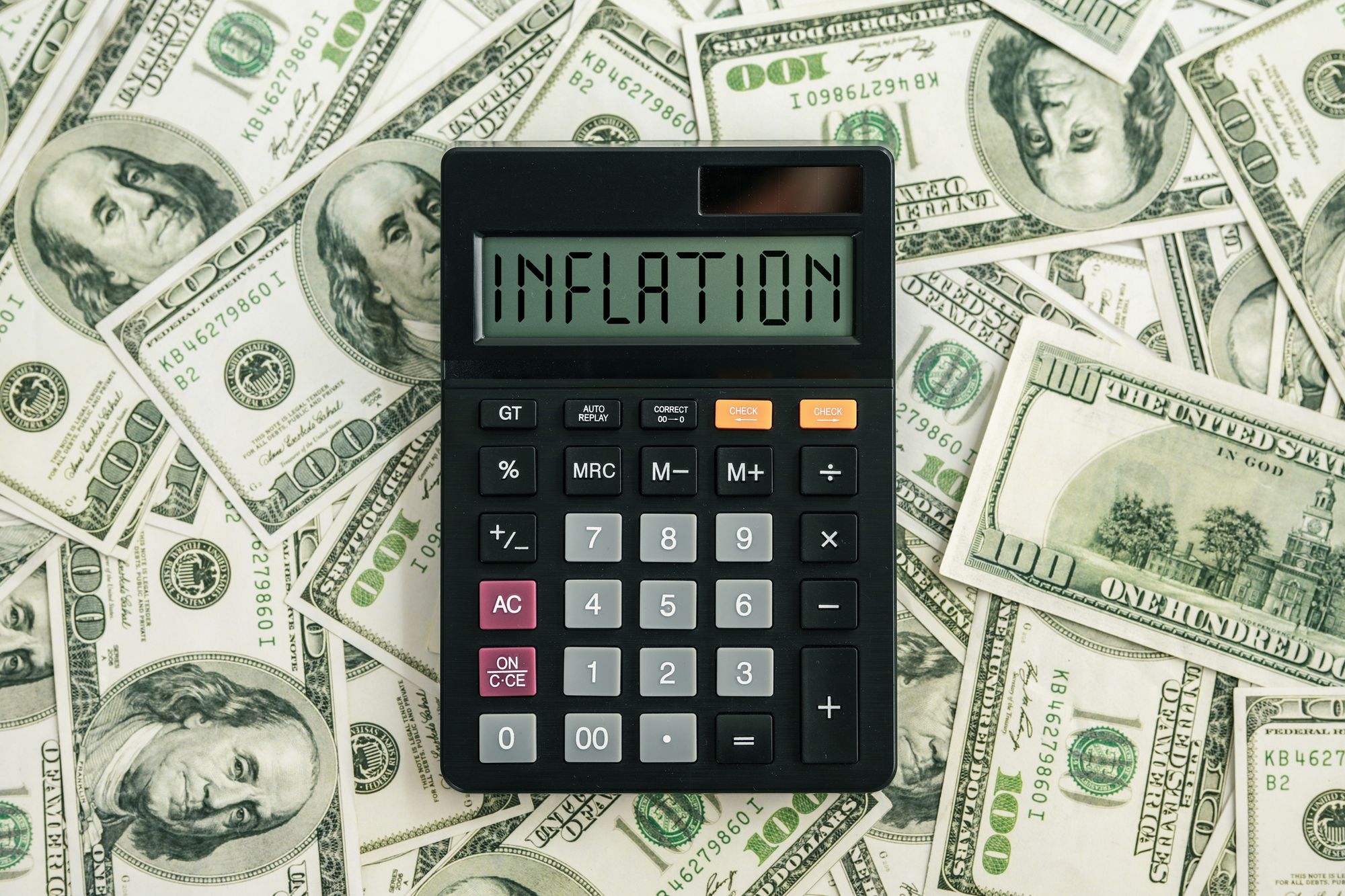 The calculator displaying the word "INFLATION" on top of 100 dollar bills