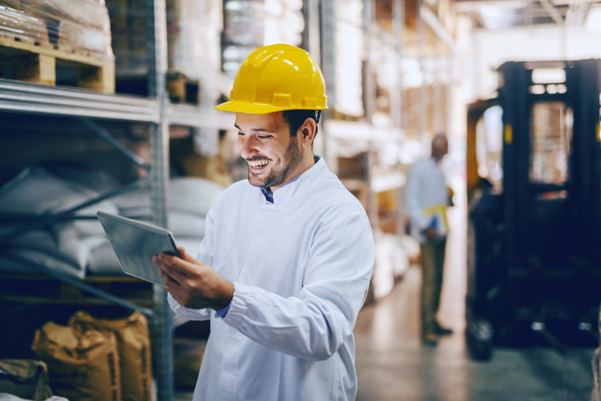A warehouse worker with a yellow hat staring at his tablet PC to check inventory.