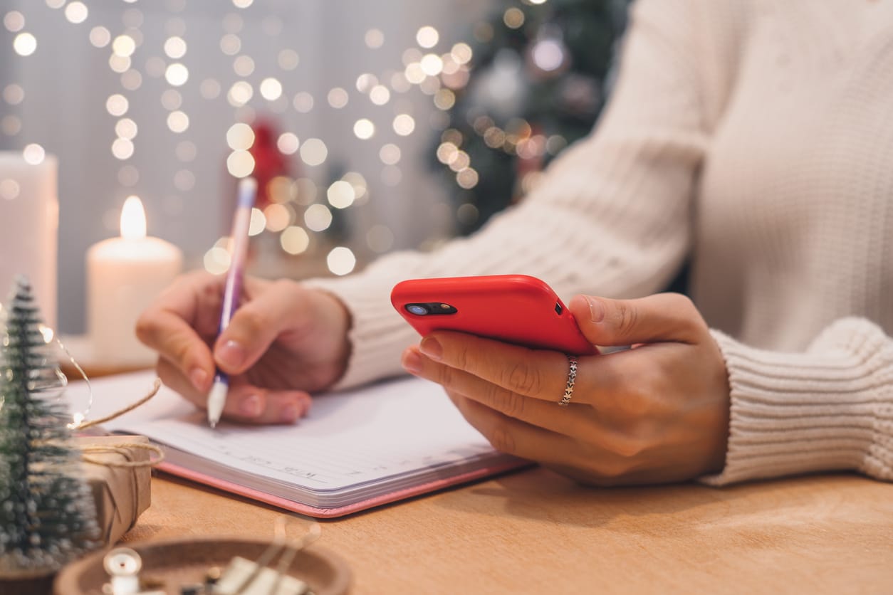 A woman's hand holding a pen on notepad and a smartphone during the holidays