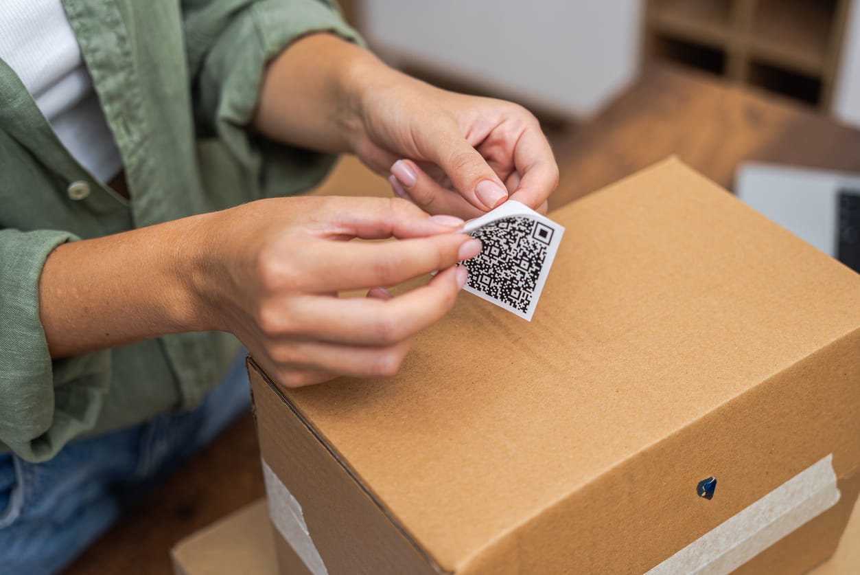 A person attaching a QR code label on a cardboard box