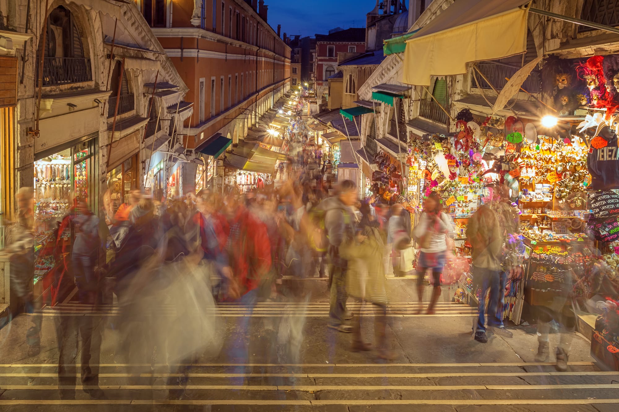 Shoppers moving through a bustling row of pop-up shops, stalls, and storefronts