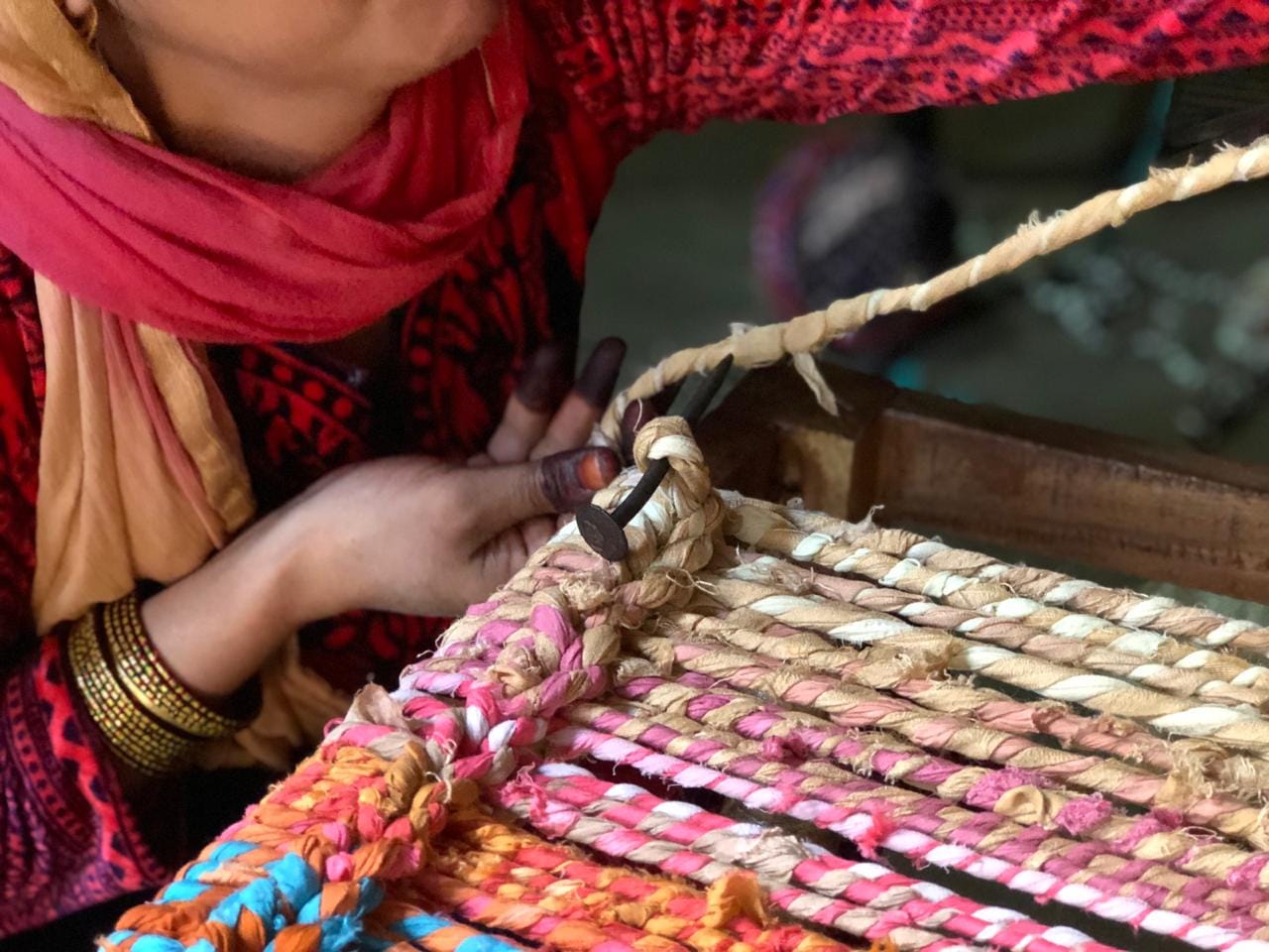 Close-up of a woman artisan weaving colorful, repurposed fabric ropes into a handmade product.