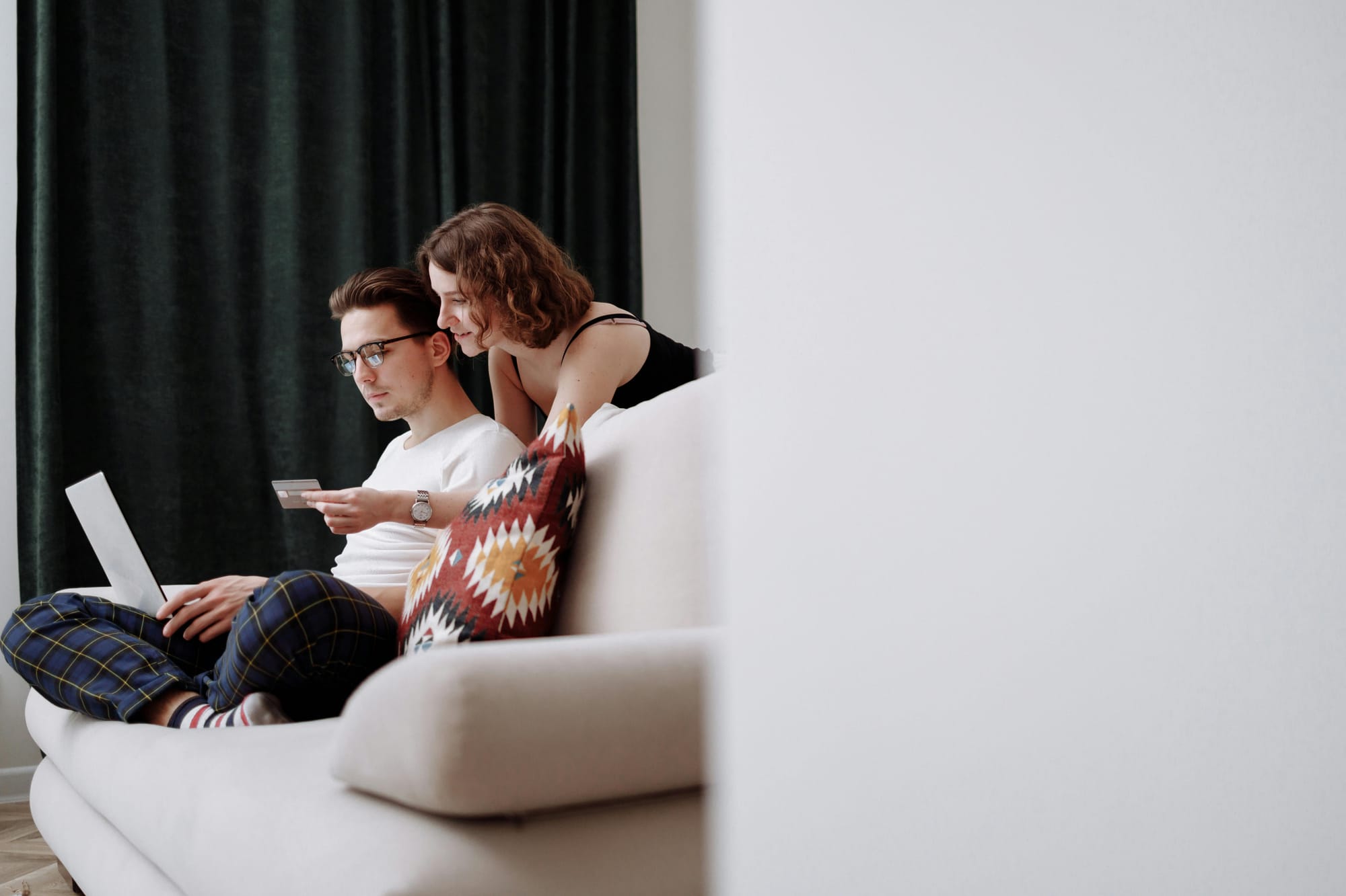 Man and woman on a couch using a laptop and credit card for online shopping.