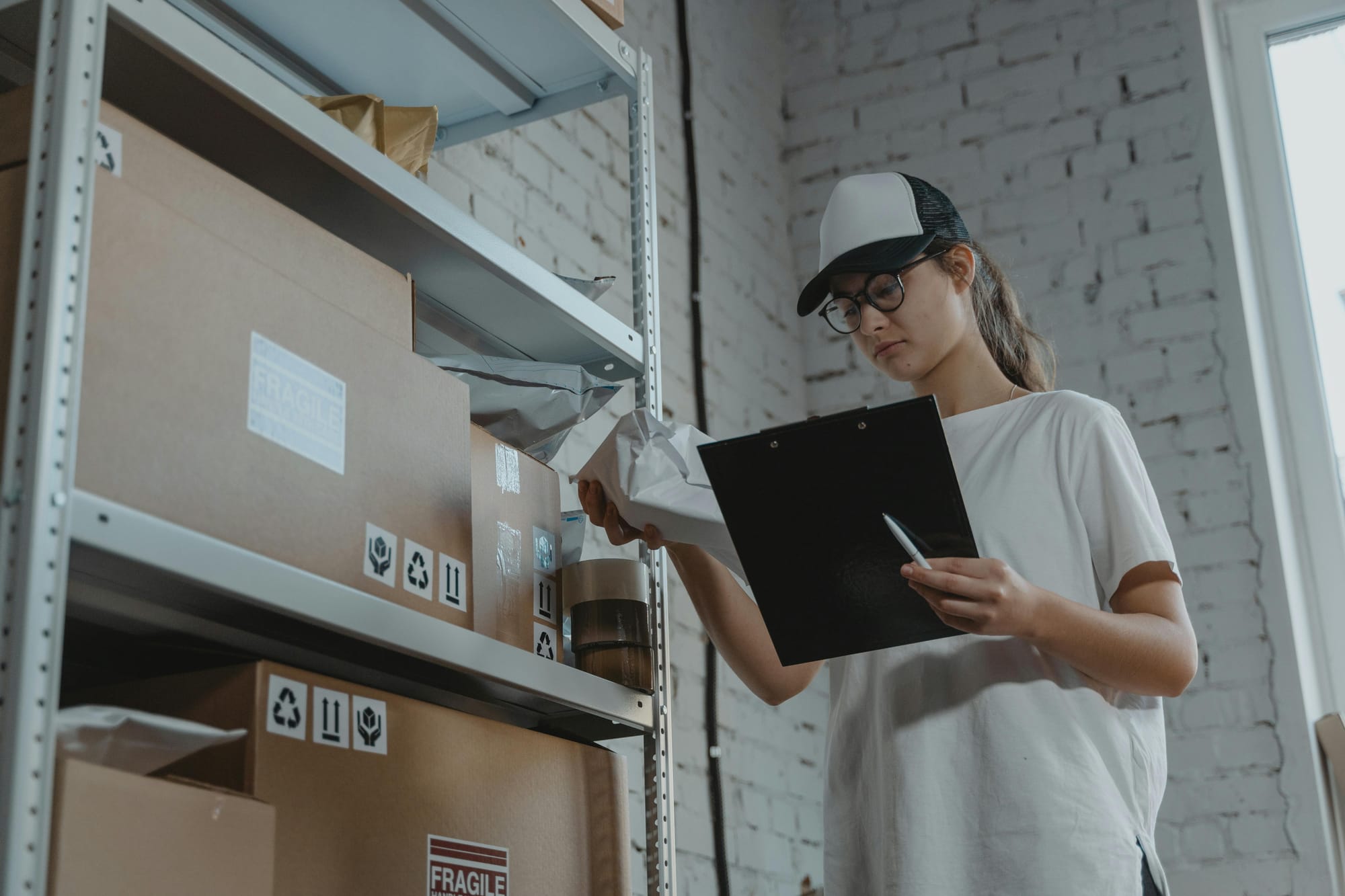 Alt text: A person holding a black clipboard in one hand and a white pack in the other, standing beside a shelf.