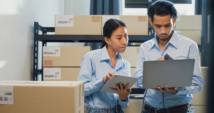 Employees looking at their laptop and tablet PC in a warehouse.