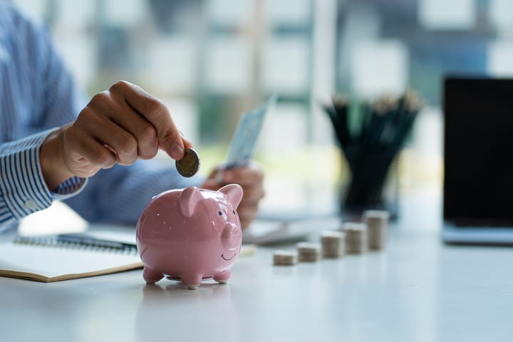 Hands of a young Asian businessman Man putting coins into piggy bank and holding money side by side to save expenses.