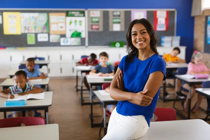 African American female teacher smiling in school classroom with students in background