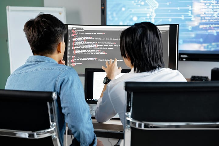 Two people collaborating in front of a computer screen displaying code.